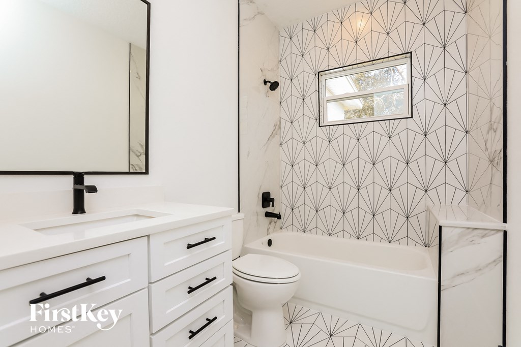 a white bathroom with geometric wallpaper and a white toilet and tub