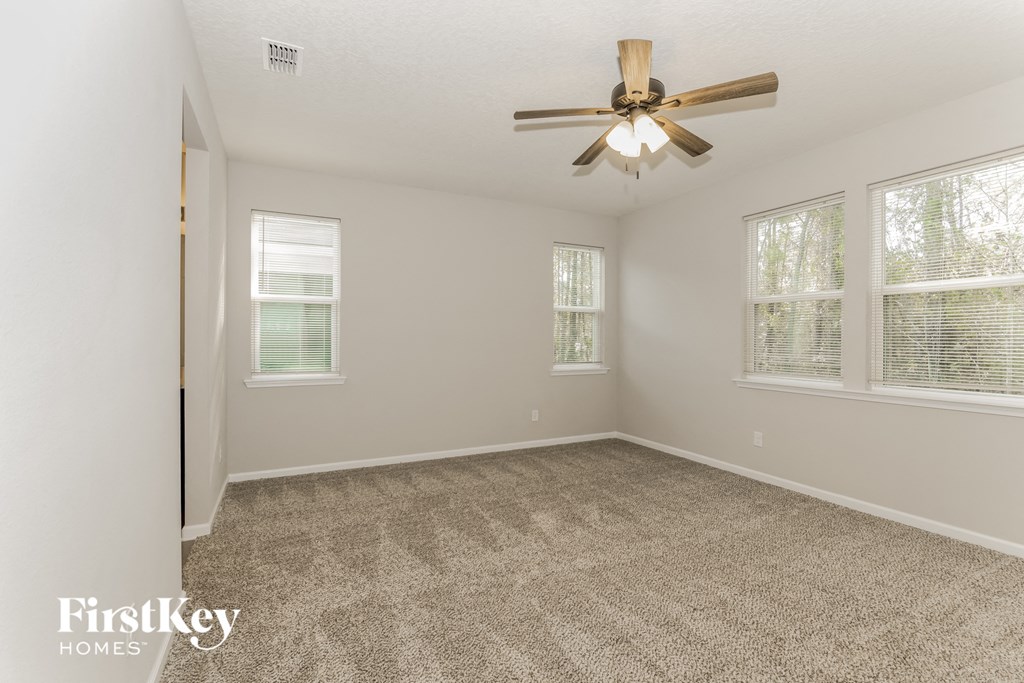 an empty living room with a ceiling fan and three windows
