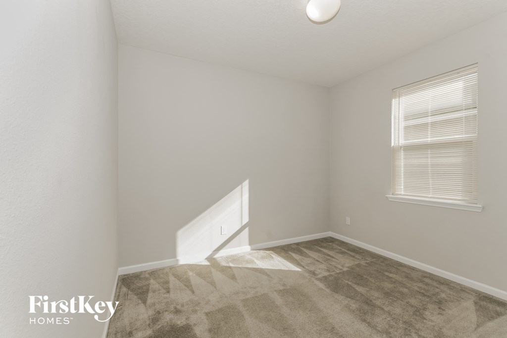a bedroom with white walls and carpet and a window