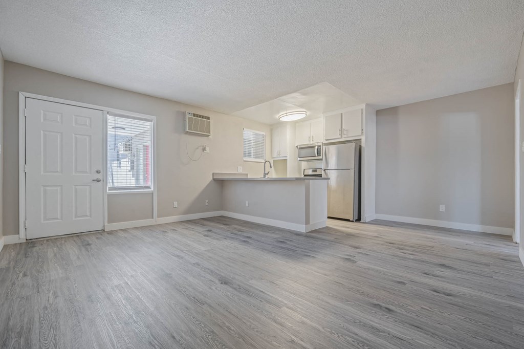 an empty living room and kitchen with a refrigerator and a sink