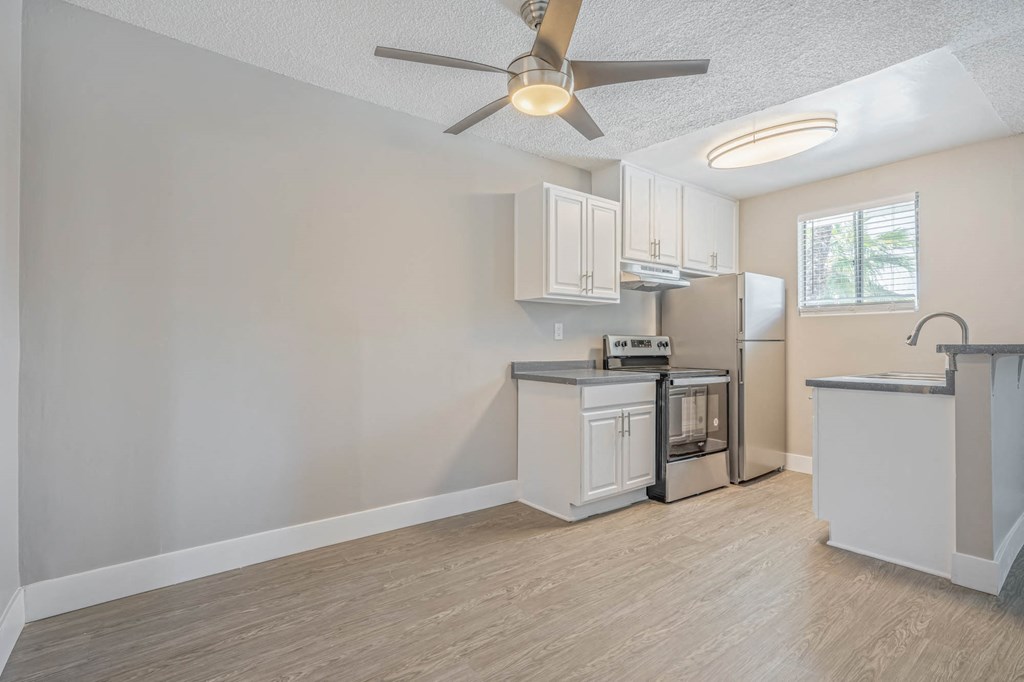 an empty living room with a kitchen and a ceiling fan