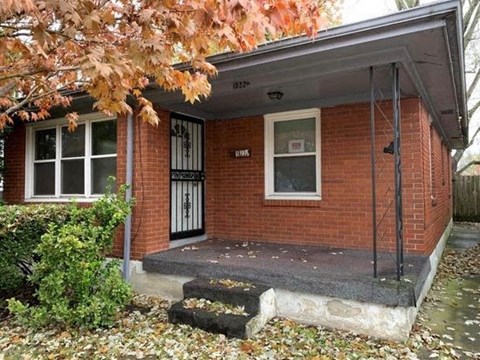 A small red brick house with a porch and a mailbox on the front door.