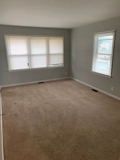 A room with carpeted floor and two windows.