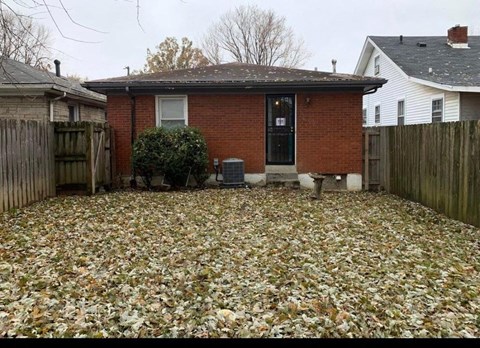 A red brick house with a black door and a black window sits in a backyard covered in leaves.