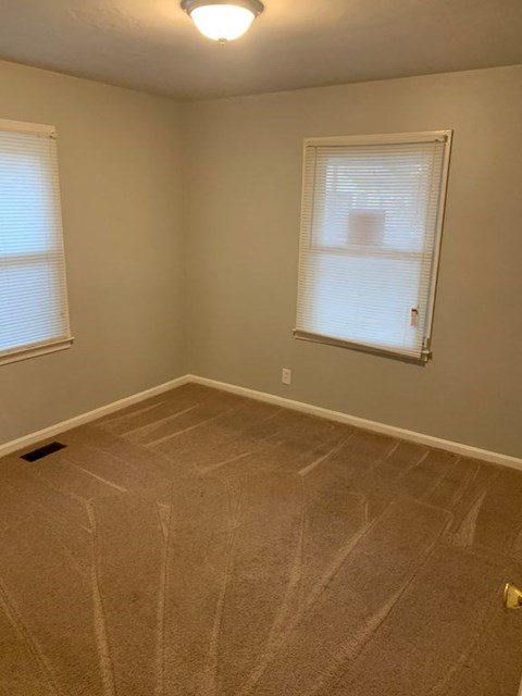 A room with a carpeted floor and a window with blinds.