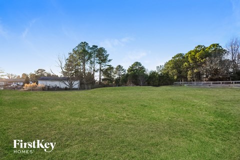 A grassy field with trees and a fence in the distance.