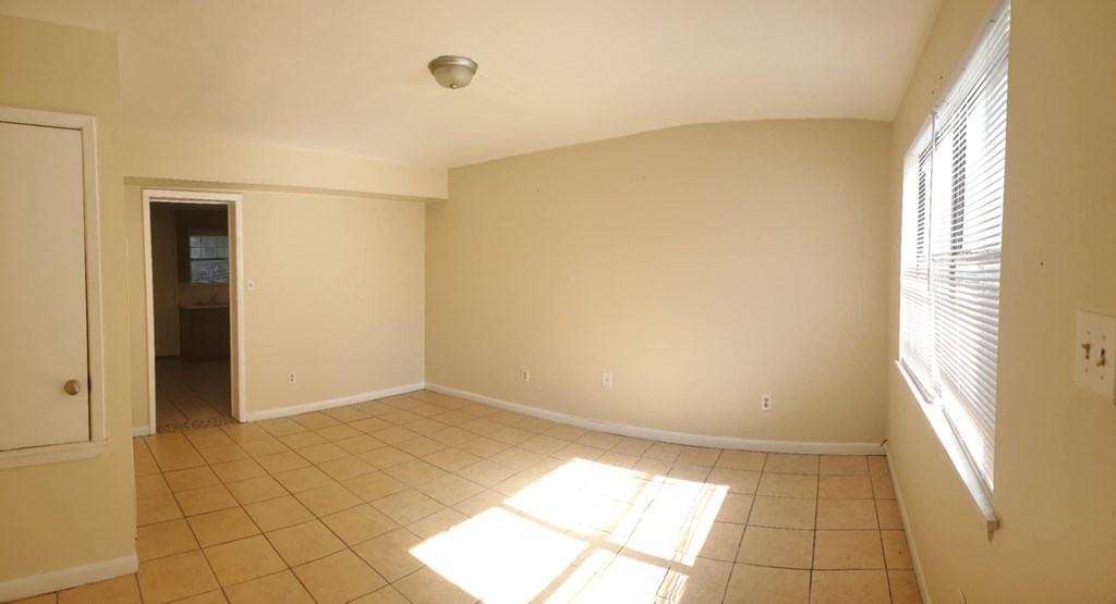 A sunny room with tiled flooring and a window on the right.