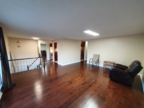 A living room with a black leather couch and wooden floors.
