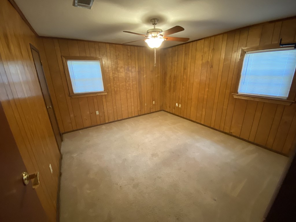 an empty room with a ceiling fan and two windows