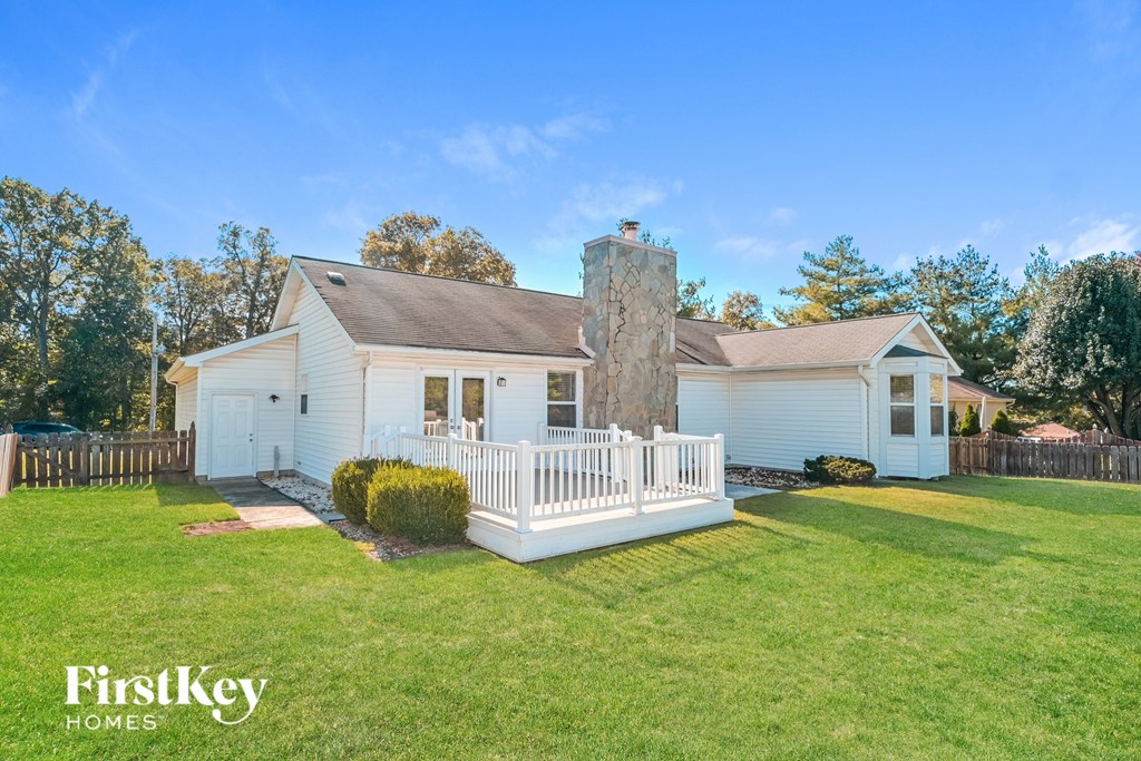 A white house with a chimney and a porch is surrounded by a green lawn.