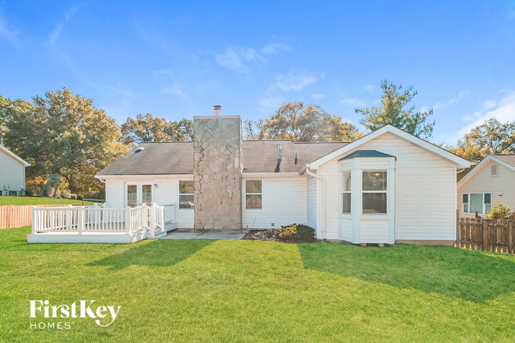 A white house with a brown roof and a chimney is surrounded by a green lawn.