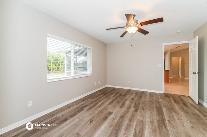 the spacious living room with hardwood flooring and a ceiling fan