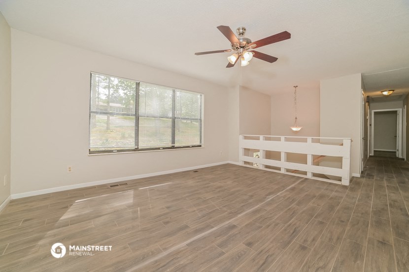 the spacious living room with a large window and a ceiling fan