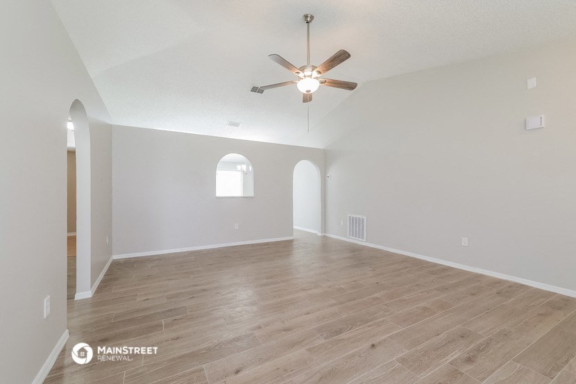the spacious living room with hardwood flooring and a ceiling fan