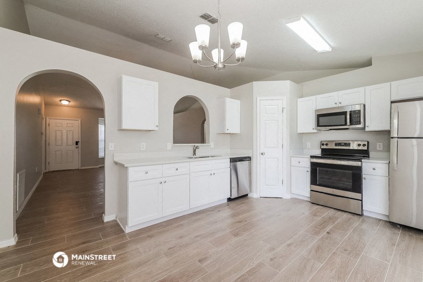 an empty kitchen with white cabinets and appliances and a wooden floor