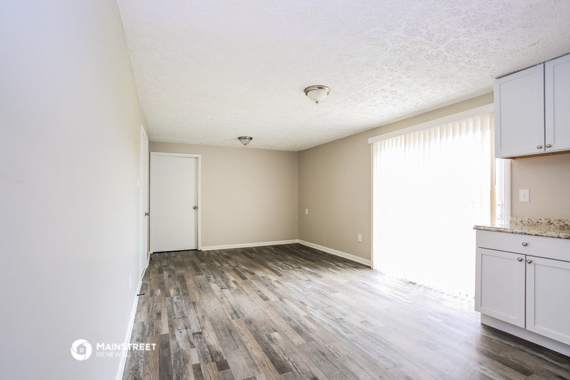 an empty kitchen and living room with wood floors and white cabinets