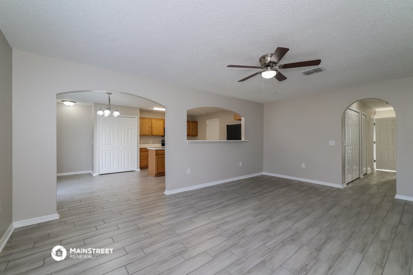 an empty living room with a ceiling fan and a kitchen