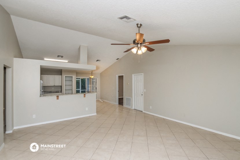 an empty living room with a ceiling fan and a kitchen