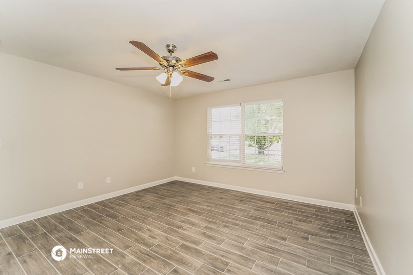the spacious living room with wood flooring and a ceiling fan