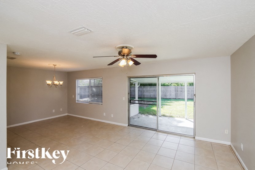 A spacious room with a ceiling fan and sliding glass doors leading to a backyard.