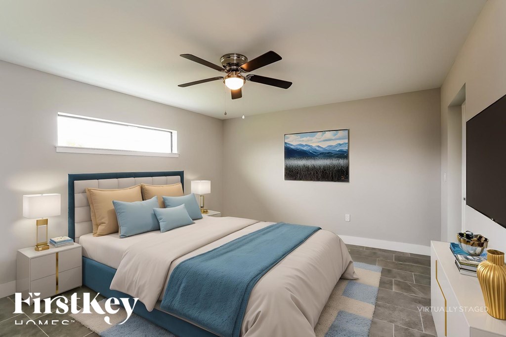 A bedroom with a bed, a ceiling fan, and a painting on the wall.