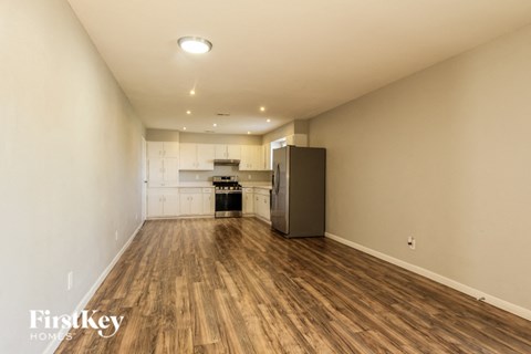 A spacious room with wooden flooring and a kitchenette in the background.