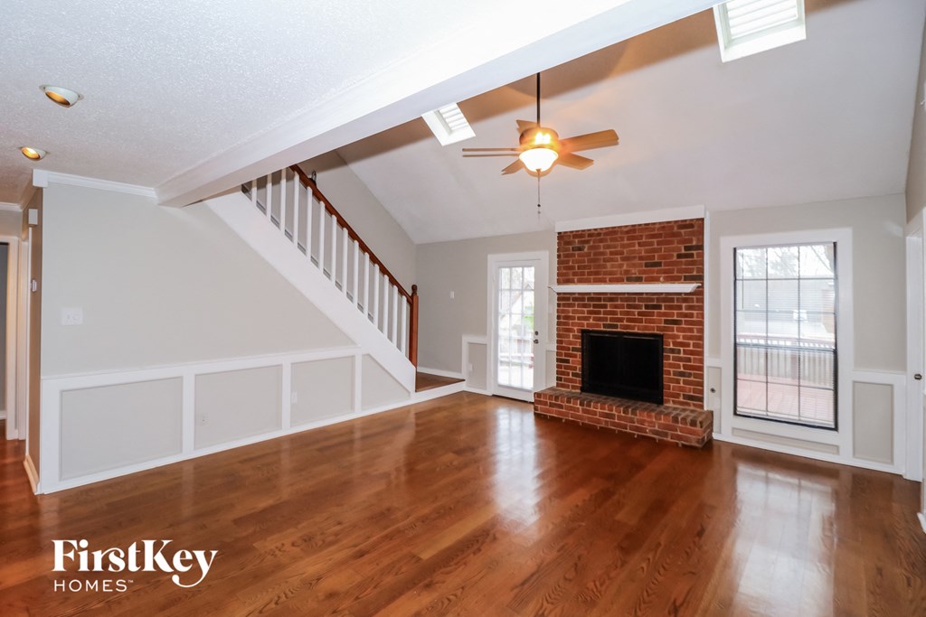 an empty living room with a brick fireplace and a ceiling fan