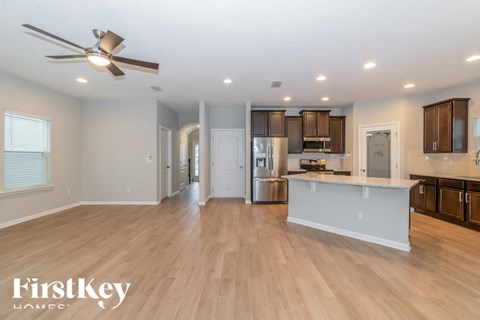 A spacious kitchen and living room with wooden floors and a ceiling fan.
