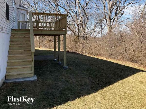 A wooden deck with a staircase is in the foreground of a grassy area.