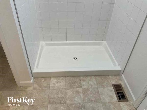 a white tiled bathroom with a shower in the floor