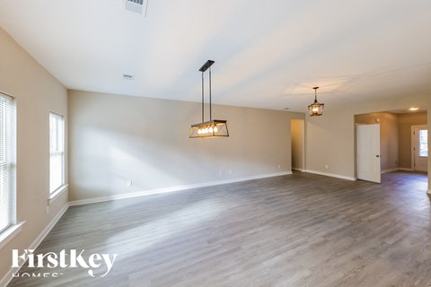 A spacious room with wooden flooring and a large window on the left side.