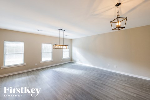 A well-lit, empty room with wooden floors and a hanging light fixture.