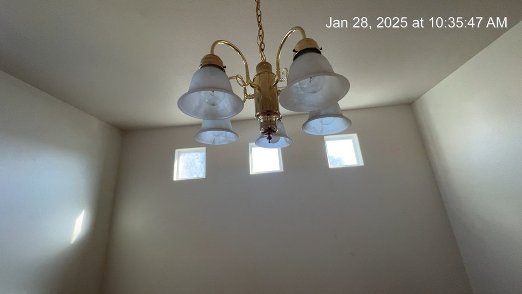 A chandelier with five lights is hanging from the ceiling in a room with white walls.