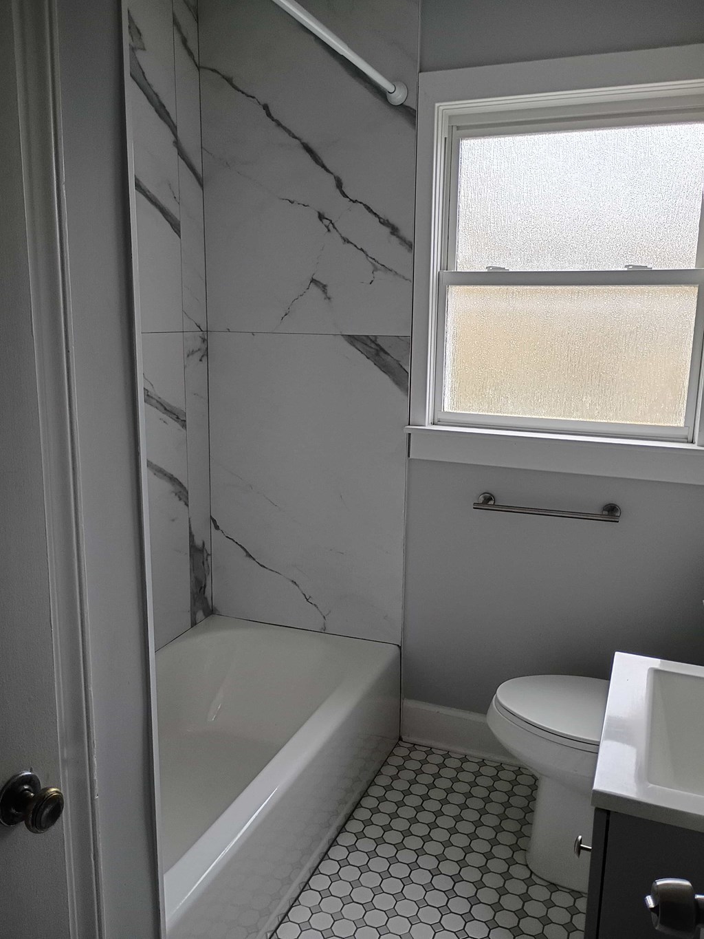 A white bathroom with a marble wall and a window.