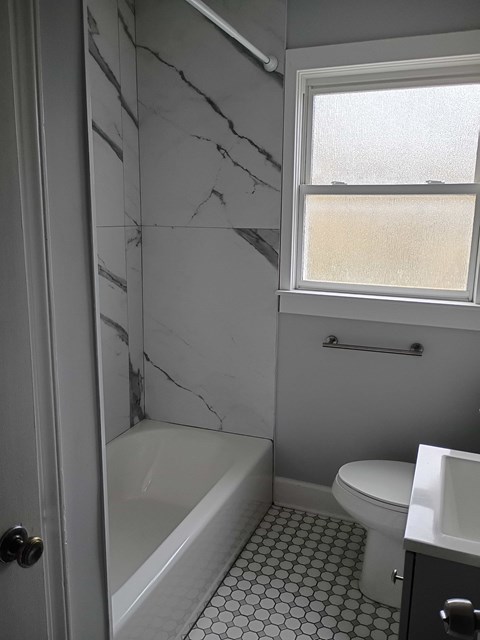 A white bathroom with a marble wall and a window.