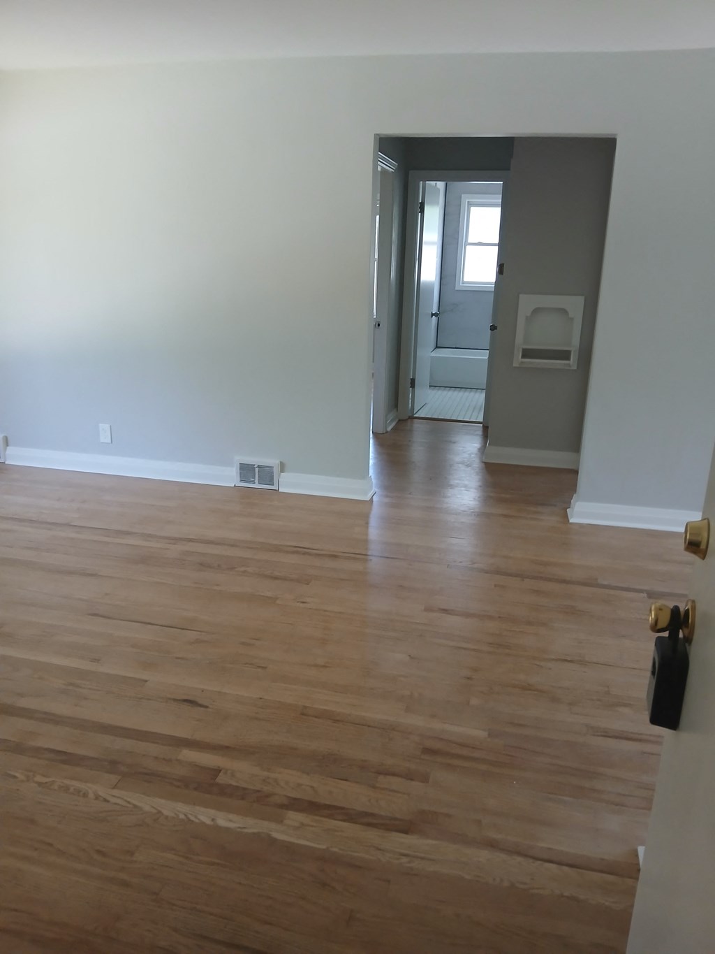an empty living room with wooden floors and a door to a hallway