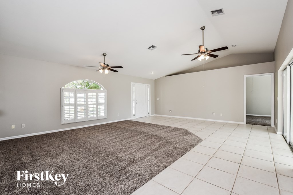 an empty living room with two ceiling fans and a rug