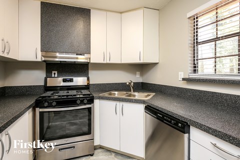 A kitchen with a stove, sink, and cabinets.