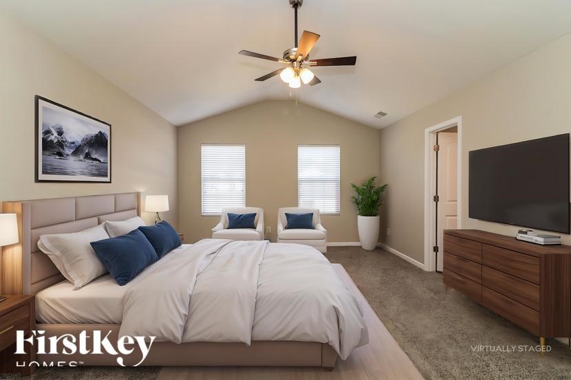 A bedroom with a large bed, a ceiling fan, and a painting on the wall.