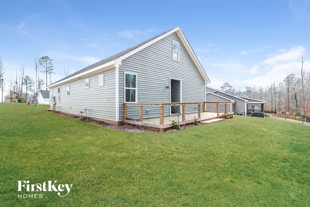 A house with a grey siding and a white trim is shown with a grassy lawn in front.