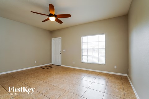 an empty living room with a ceiling fan and tiled floors