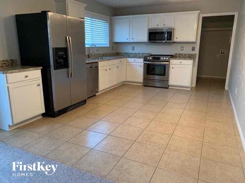 A kitchen with a black fridge, white cabinets, and a tiled floor.