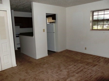 an empty living room with a kitchen and a refrigerator