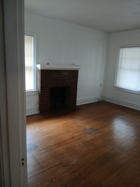 an empty living room with a brick fireplace and wooden floors