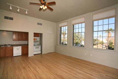 an empty living room with a kitchen and a ceiling fan
