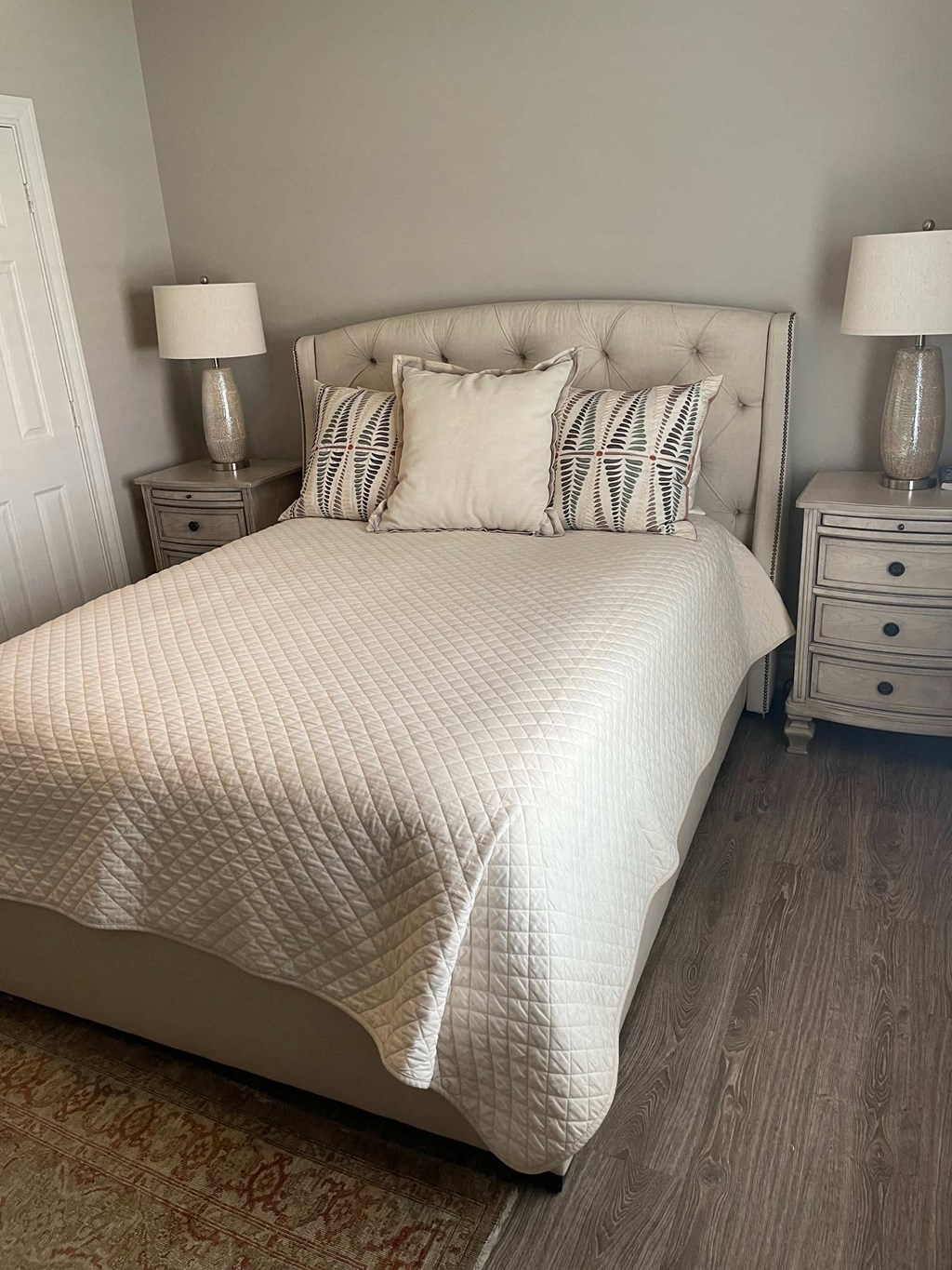 a white bed with pillows in a room with a wooden floor