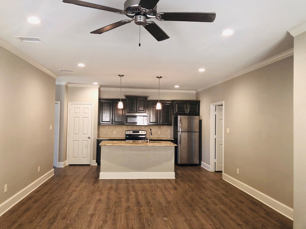 an empty living room with a kitchen and a ceiling fan