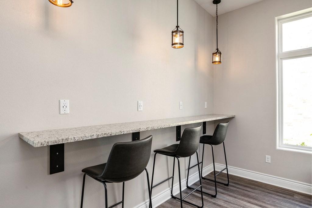 an empty kitchen with a long counter with three chairs and two hanging lights