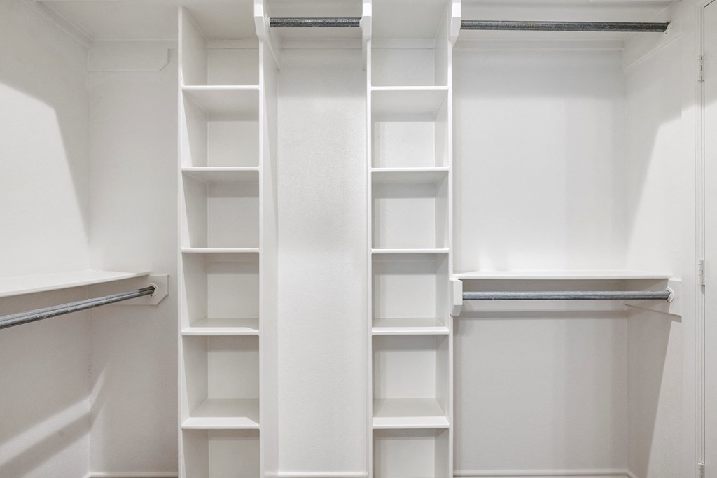a walk in closet with white shelves and