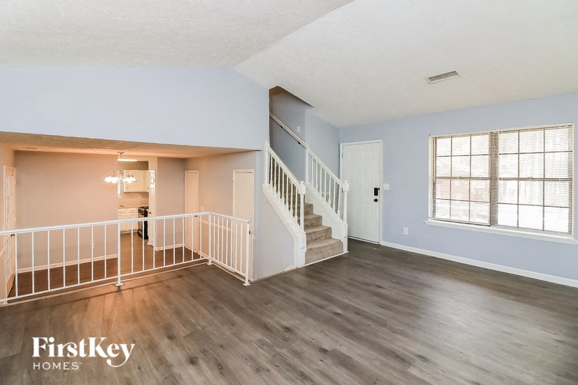 the living room and entryway of a house with wood floors and a staircase